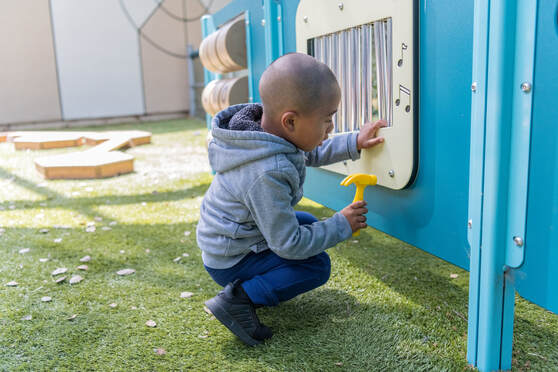 A young child pretends to fix a play structure while using a toy hammer