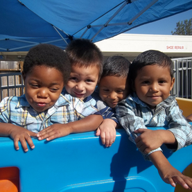 4 boys stand on top of a blue play structure, smiling with their arms around each other