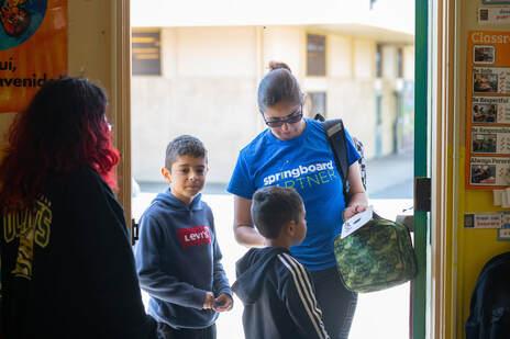 An educator stands at the door to greet students and parents at the end of the day