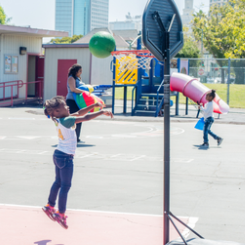 Young girl jumps up to toss a ball through a standing hoop