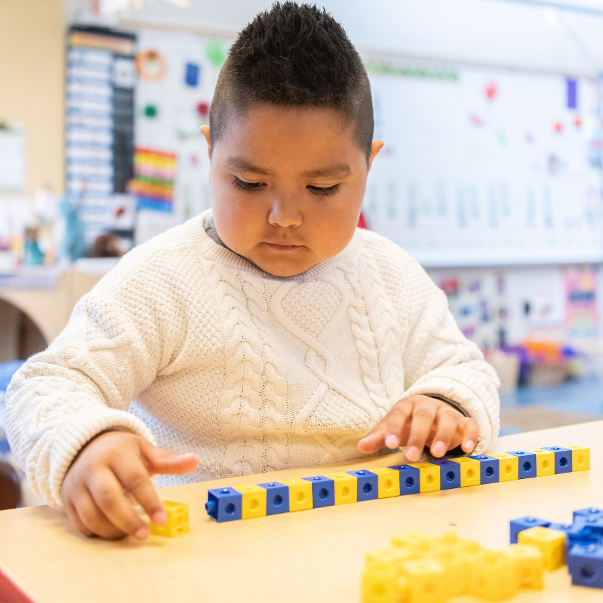 A young child with round cheeks lines up blue and yellow blocks